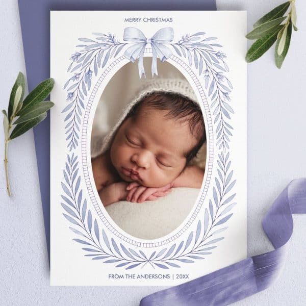 Christmas Card Featuring A Sleeping Newborn Baby In An Oval Frame Decorated With A Blue Wreath.