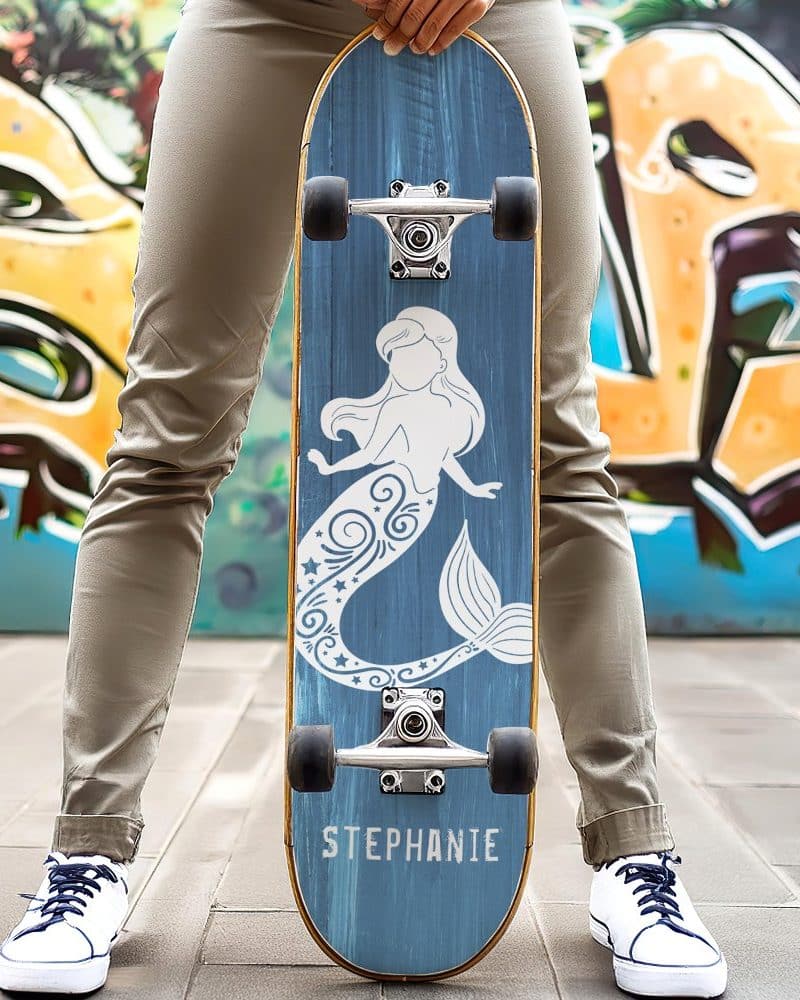 Person holding a blue skateboard with a white mermaid design and the name Stephanie.