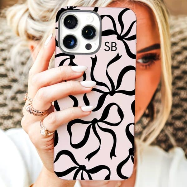 A Woman'S Hand Holds Up A Pink Iphone Case Covered In A Pattern Of Black Bows.
