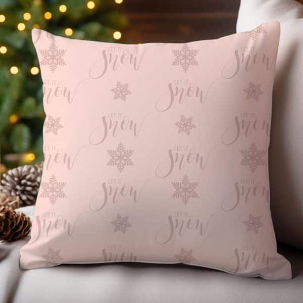 Pink Decorative Pillow With A Repeating Pattern Of Snowflakes And The Words Let It Snow.