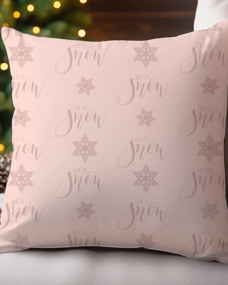 Pink decorative pillow with a repeating pattern of snowflakes and the words Let it Snow.