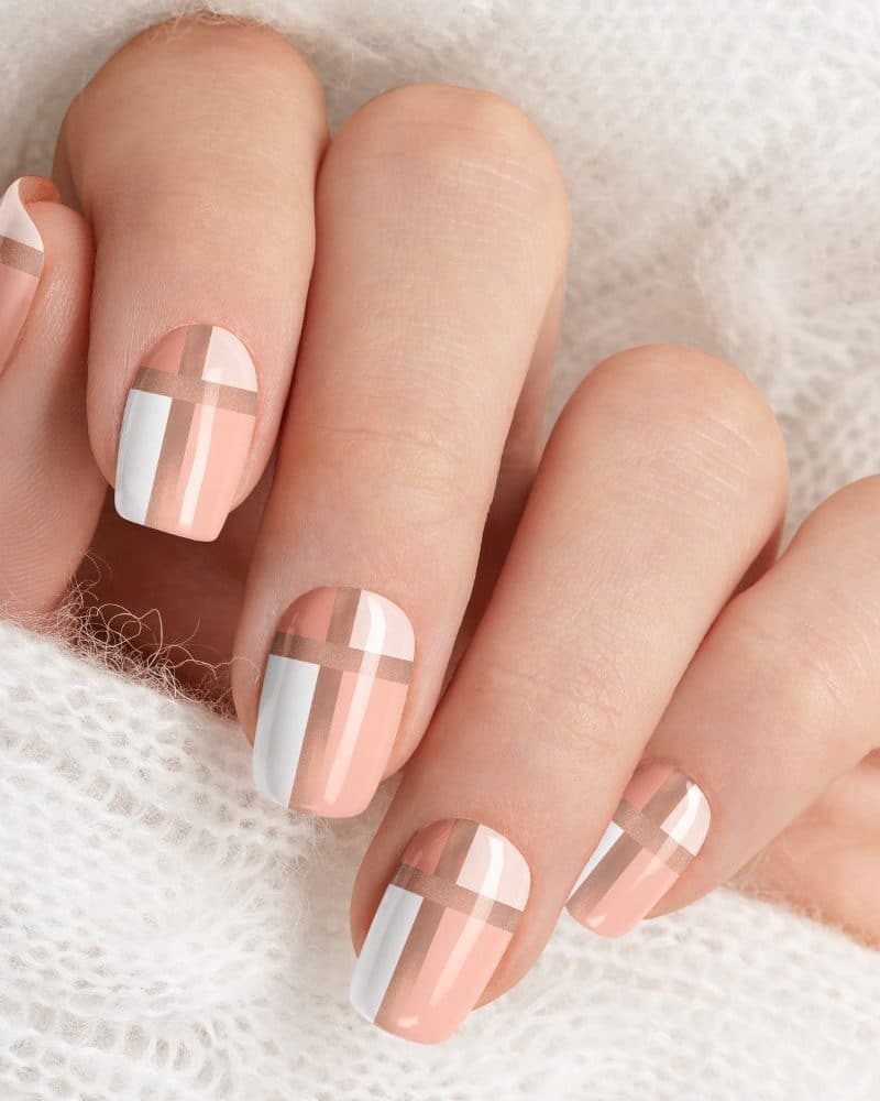 Close-up of a hand with nails painted in a peach and white plaid design.