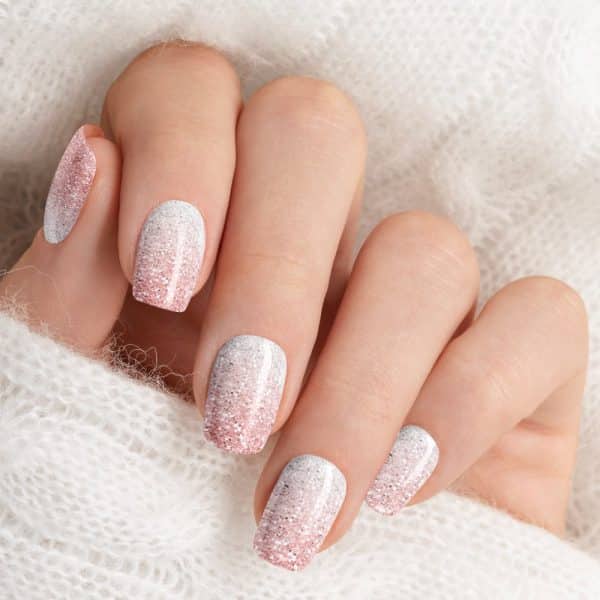 Close Up Of A Hand With Nails Painted A Sparkly Ombre Design Transitioning From Pink To White.