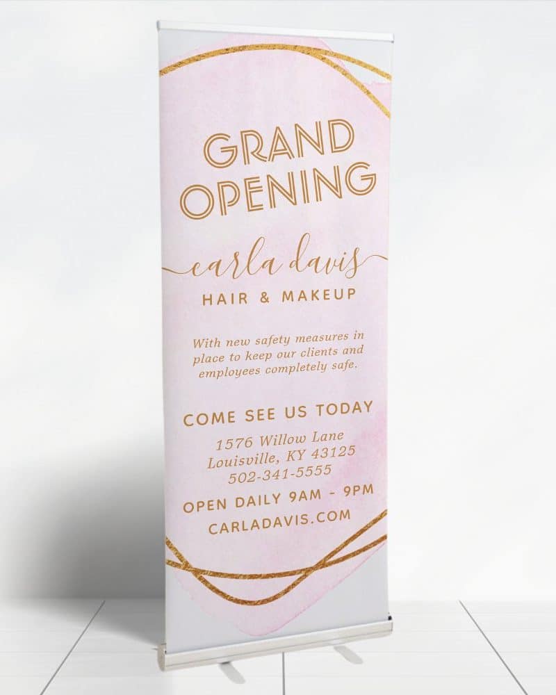 Grand opening retractable banner for Carla Davis Hair & Makeup. The banner features a pink watercolor design with gold accents. Contact information and daily hours are included.