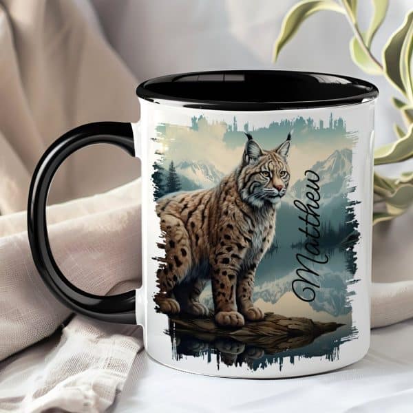 A Black And White Coffee Mug Featuring A Lynx Sitting On A Rock By A Lake, With Mountains In The Background. The Name Matthew Is Printed On The Mug.