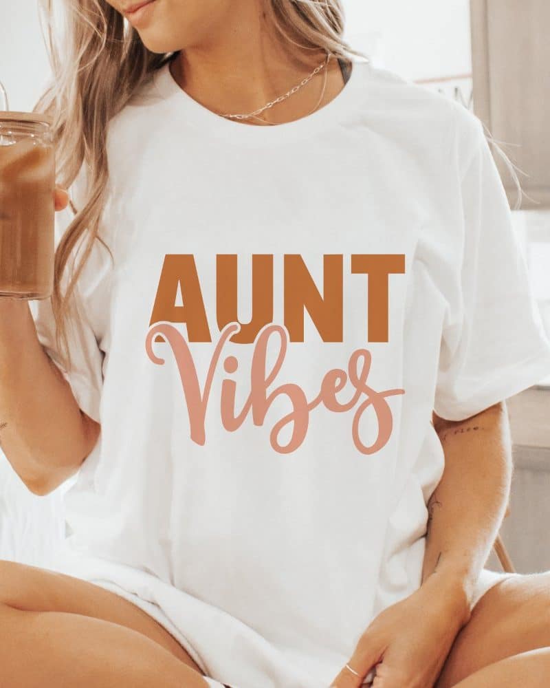 Woman wearing a white t-shirt that says Aunt Vibes in brown and pink lettering.