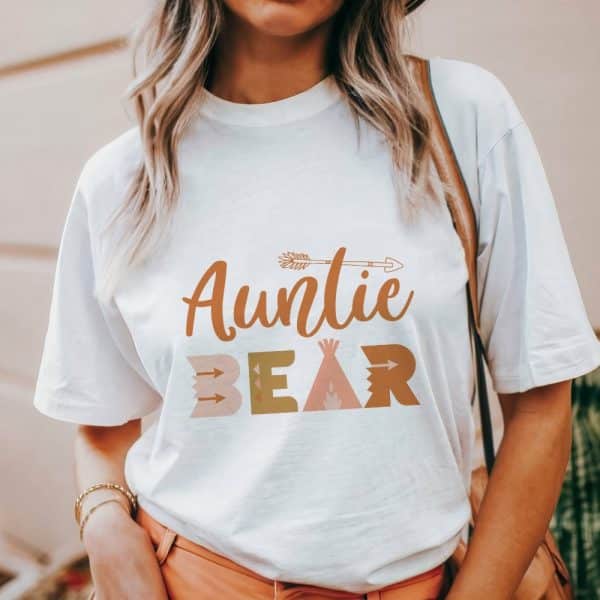 Woman Wearing A White T-Shirt That Says Auntie Bear In A Boho-Style Font.
