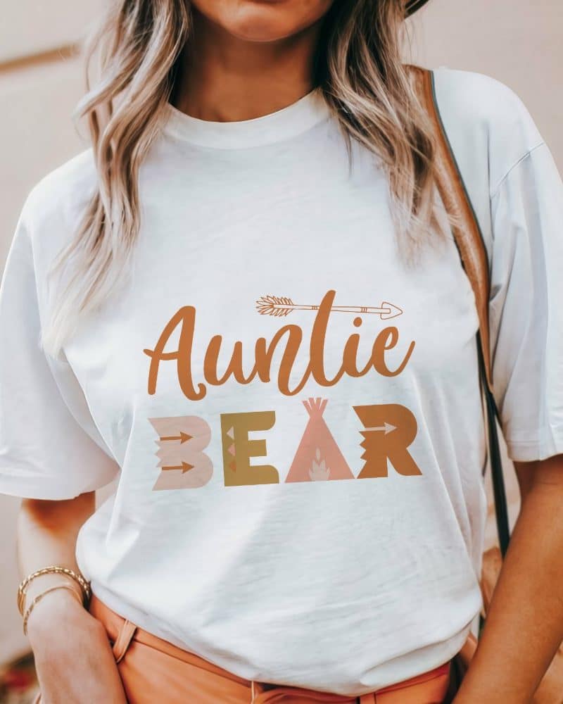 Woman wearing a white t-shirt that says Auntie Bear in a boho-style font.
