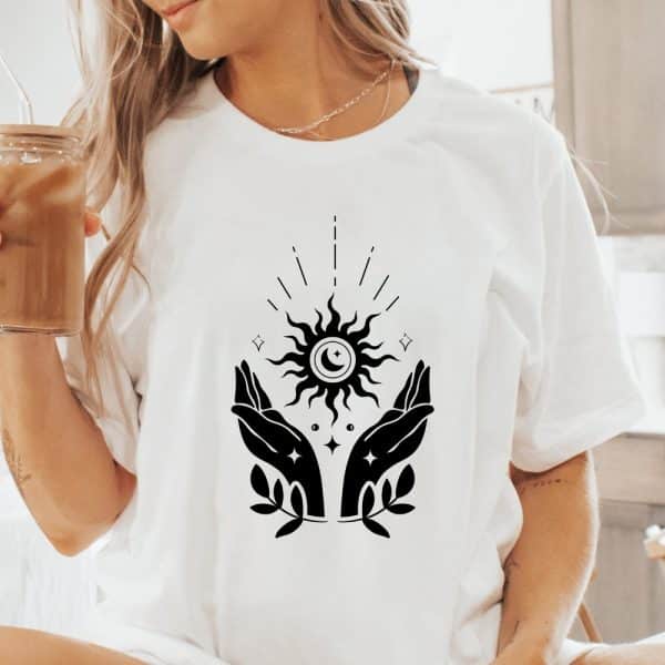 White T-Shirt With A Black Design Of Two Hands Cradling A Sun And Moon.