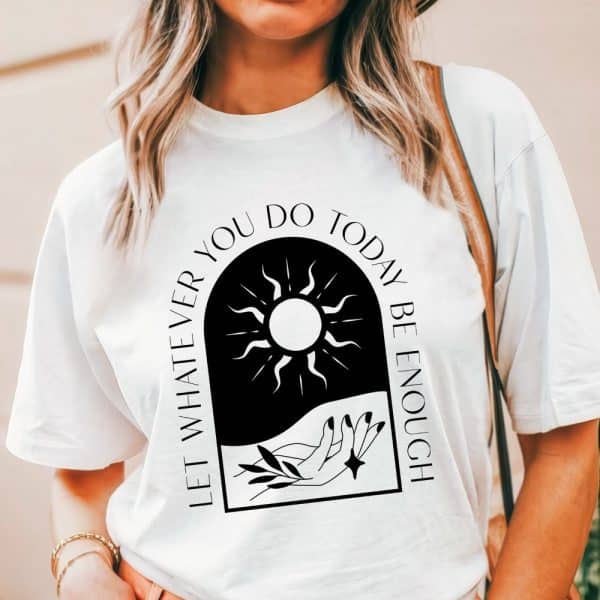 White T-Shirt With A Black Arched Graphic Design. The Design Features A Sun, A Hand, And Leaves, And The Text Let Whatever You Do Today Be Enough.