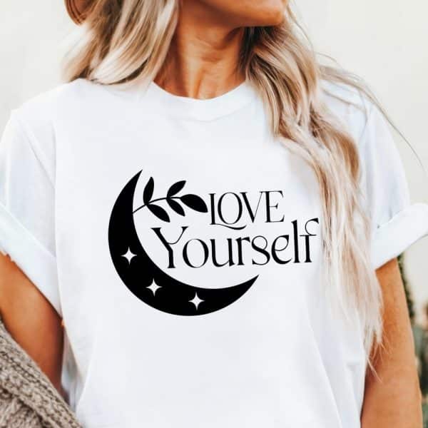 White T-Shirt With A Black Crescent Moon, Leaves, And The Words Love Yourself.