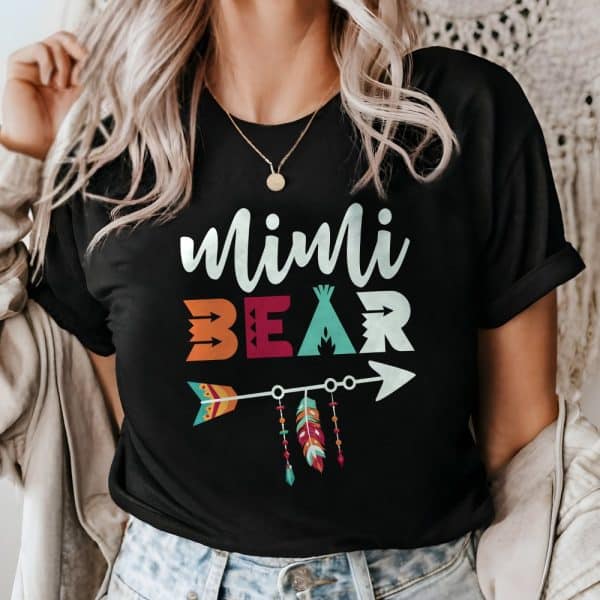 Woman Wearing A Black T-Shirt That Says Mimi Bear In Colorful Letters With An Arrow And Feathers Design.