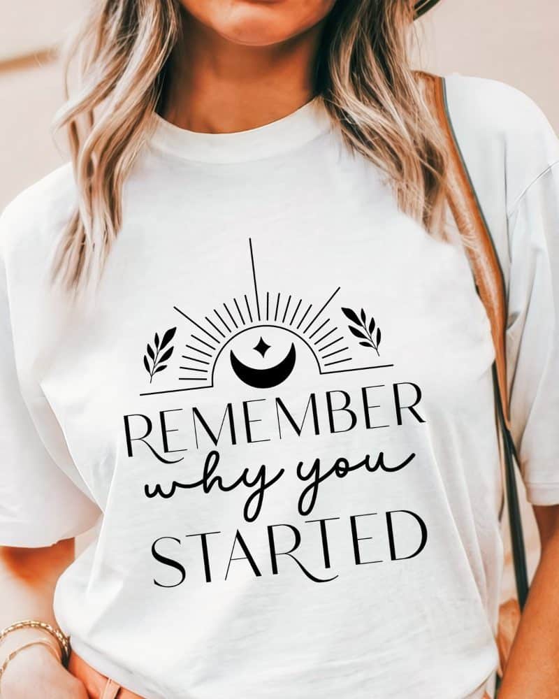 White t-shirt with the text Remember why you started, centered, in a stylized font with a sun and moon graphic above.