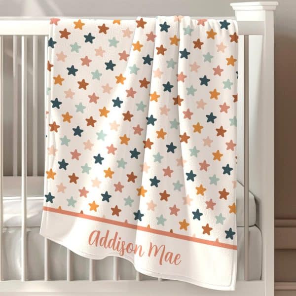 Personalized Baby Blanket With A Star Pattern In Muted Orange, Pink, Teal, And Blue.