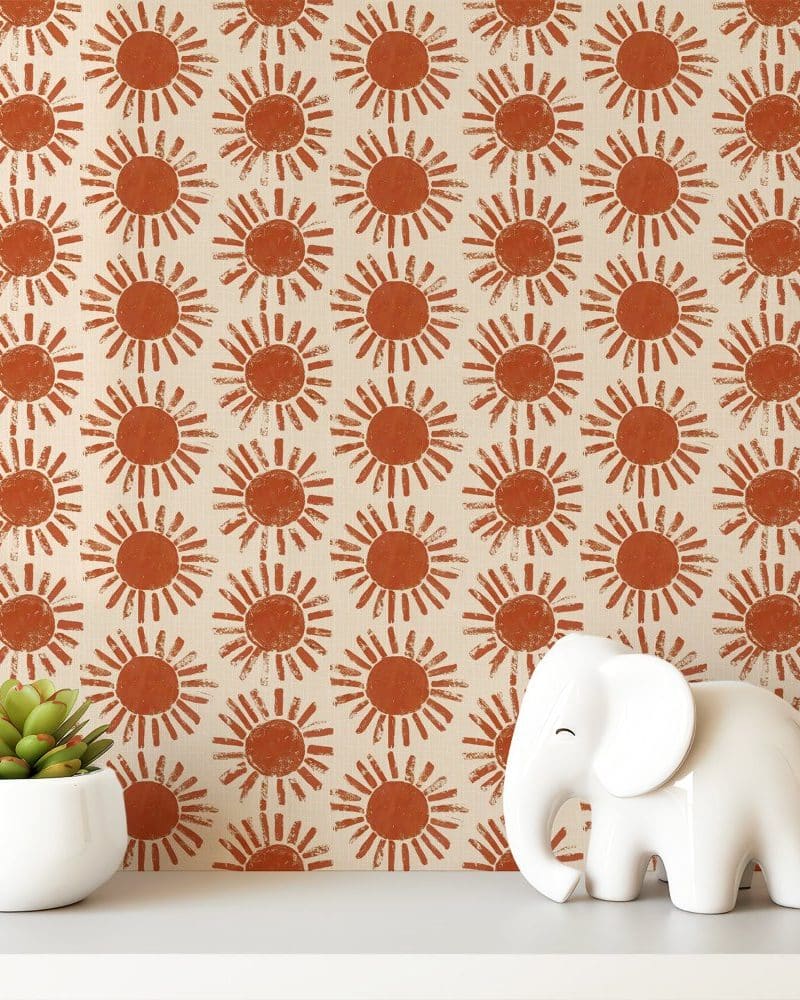 A white shelf displays a small potted succulent and a white elephant figurine against a background of wallpaper featuring a repeating pattern of burnt orange suns.