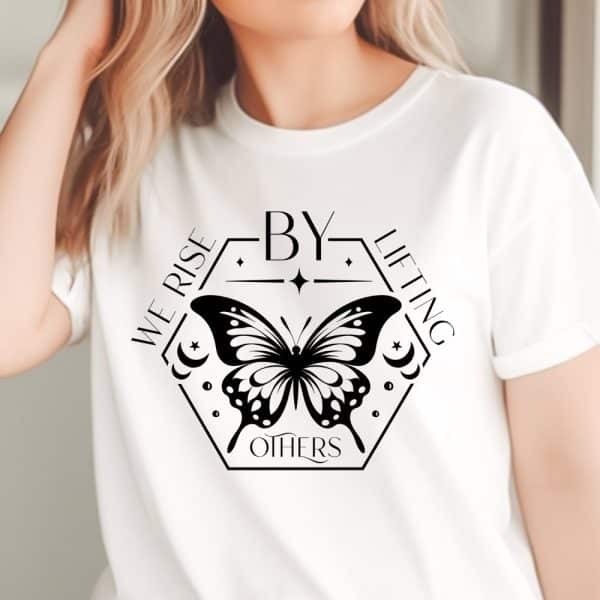 White T-Shirt With A Black Butterfly Design Centered On The Chest. The Butterfly Is Inside A Hexagon With The Words We Rise By Lifting Others.