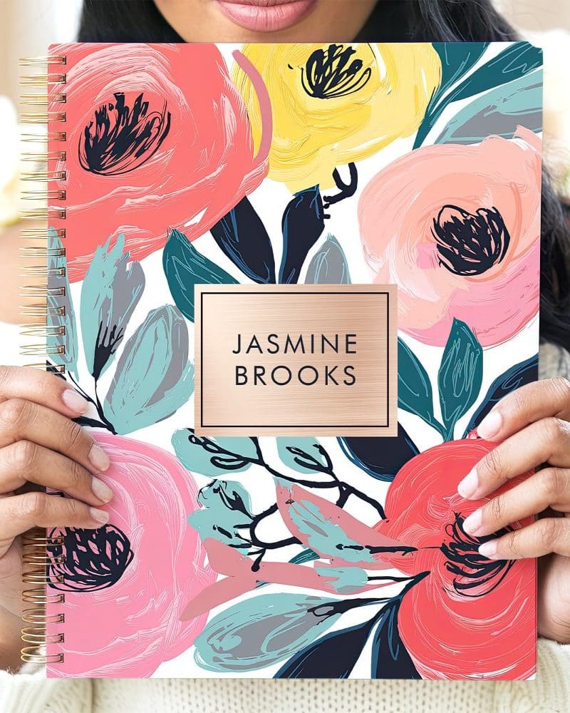 A woman's hands hold a spiral-bound notebook with a floral design and the name Jasmine Brooks.