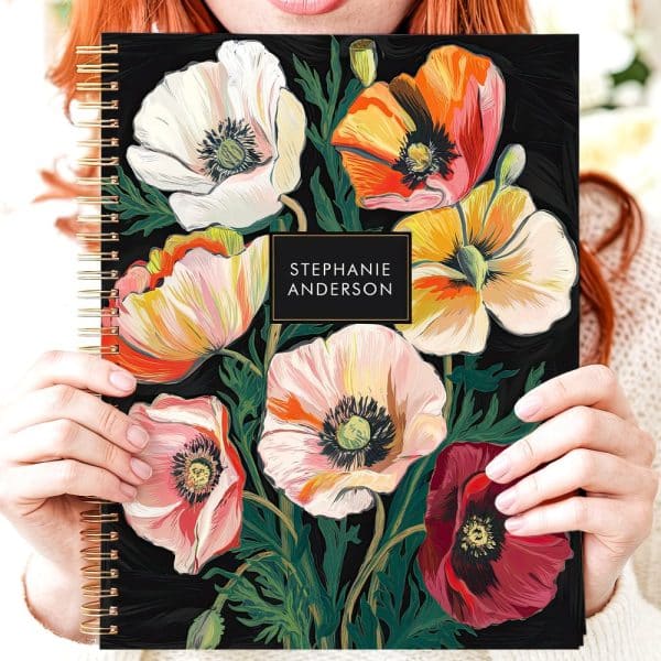 A Woman Holds A Spiral-Bound Notebook Featuring A Dark Background And A Colorful Floral Design Of Poppies. The Name Stephanie Anderson Is Printed On The Cover.