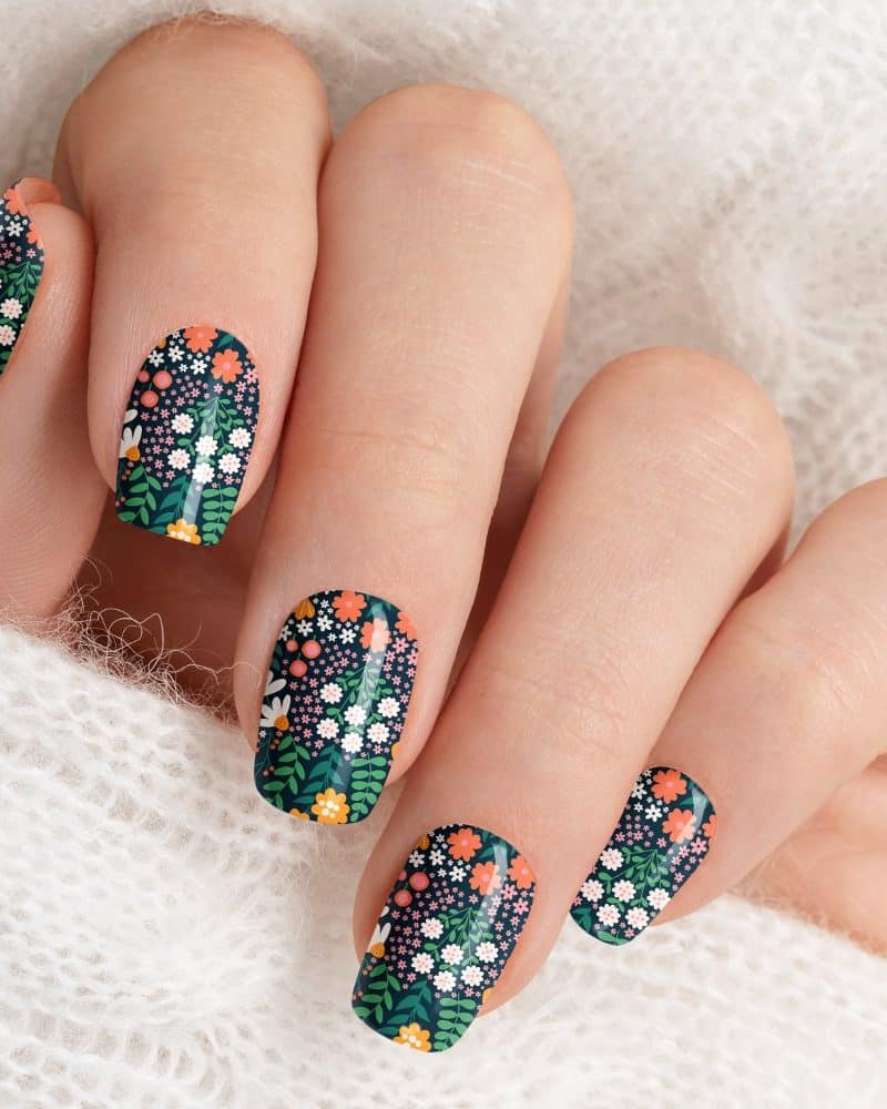 Close-up of a hand with fingernails adorned with dark green floral nail art.