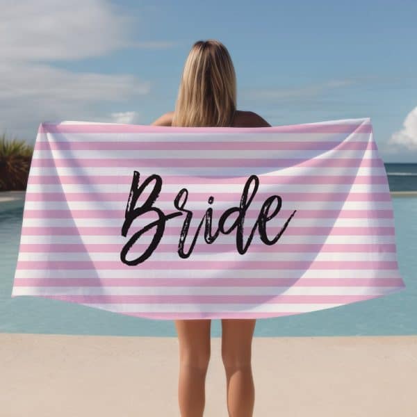 A Woman Holds A Pink And White Striped Beach Towel That Says Bride In Black Lettering.
