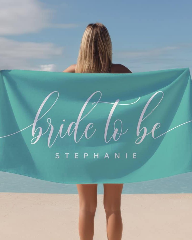 Woman holding a teal beach towel that says Bride to be Stephanie.