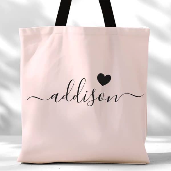 Pink Tote Bag With The Name Addison In Black Script Lettering And A Small Black Heart.