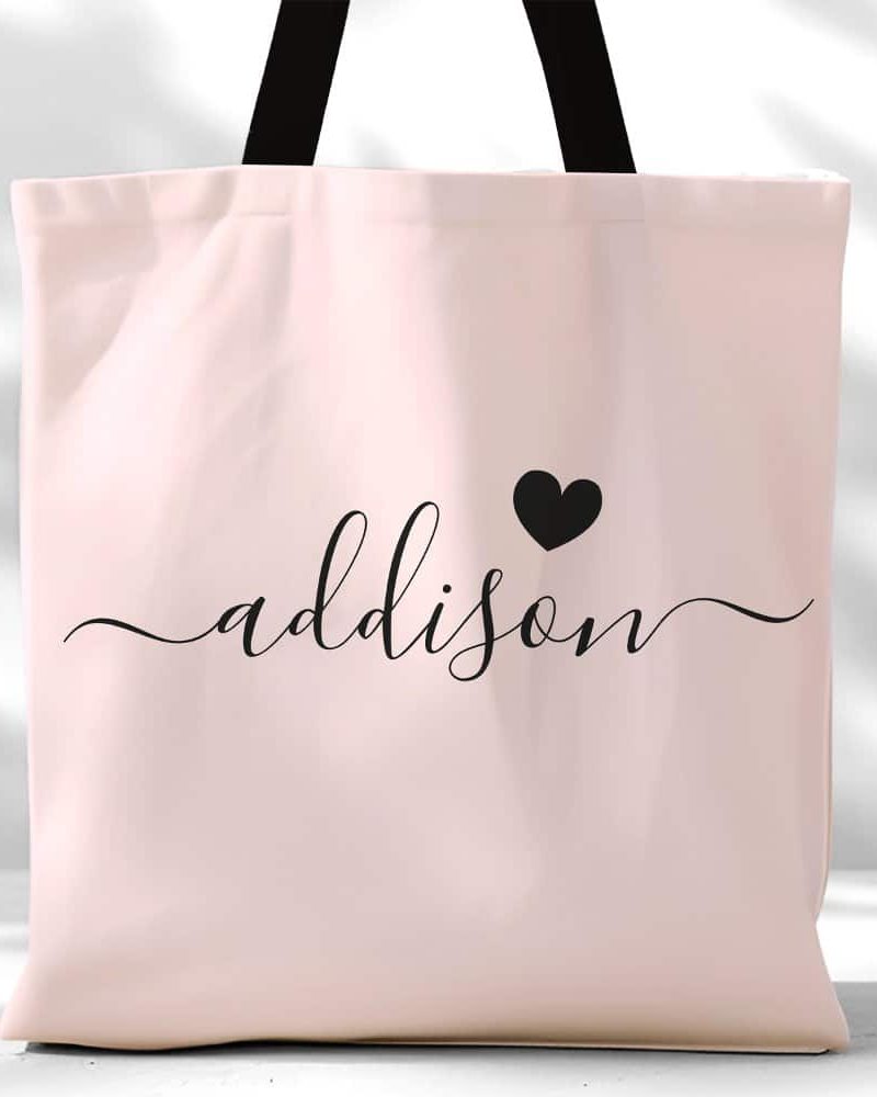 Pink tote bag with the name Addison in black script lettering and a small black heart.