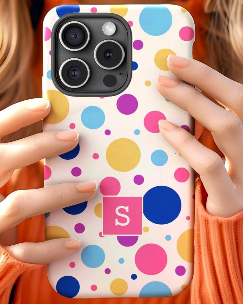 Close-up of hands holding a phone in a colorful polka dot case with a pink initial S.
