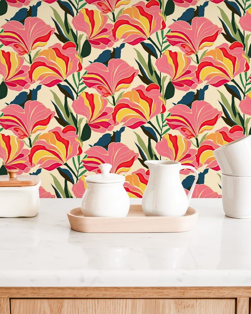 White kitchenware sits on a marble countertop in front of a floral wallpaper featuring stylized pink, red, and yellow flowers on a cream background.