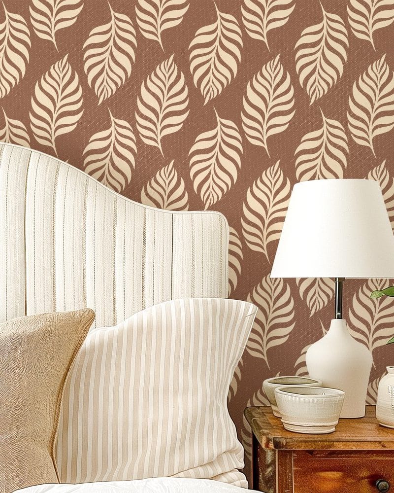 A bedroom headboard and pillows against a wall with a repeating leaf pattern wallpaper.