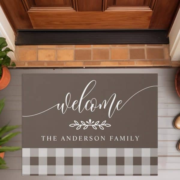 A Welcome Mat With The Text Welcome The Anderson Family. The Mat Is Brown With A White Script Font And A Gingham Bottom Border.