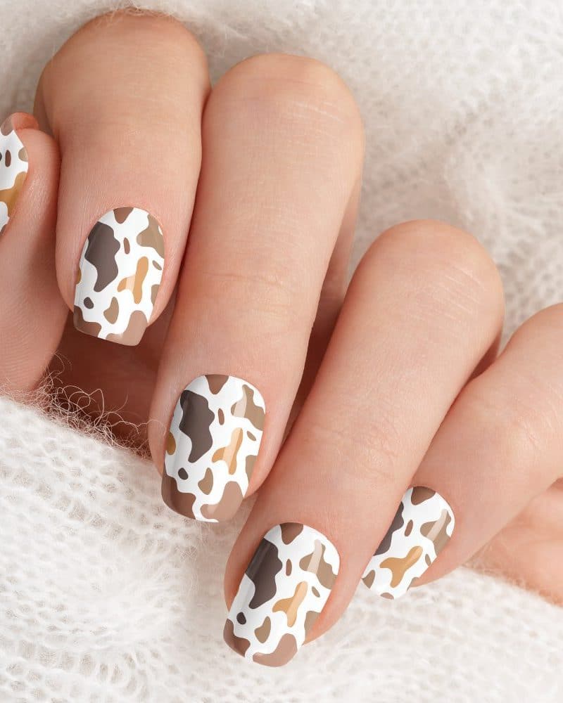 Close-up of a hand with fingernails painted with a cow print design in brown and beige.