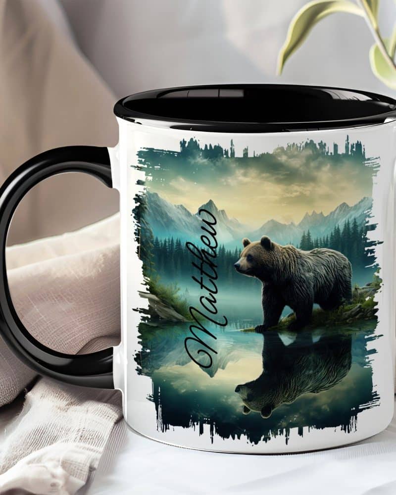 A black-handled mug with a personalized name, Matthew, and a grizzly bear reflected in a mountain lake.