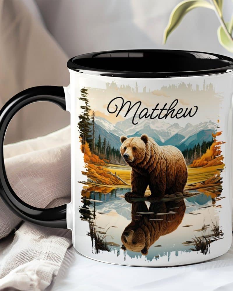 Personalized coffee mug with a grizzly bear reflected in calm water, mountains in the background, and the name Matthew.