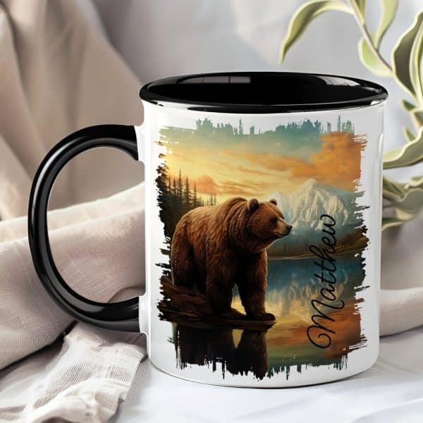 A Coffee Mug With A Black Handle And Interior Features A Grizzly Bear Standing By A Lake At Sunset, With Mountains In The Background. The Name Matthew Is Printed On The Mug.