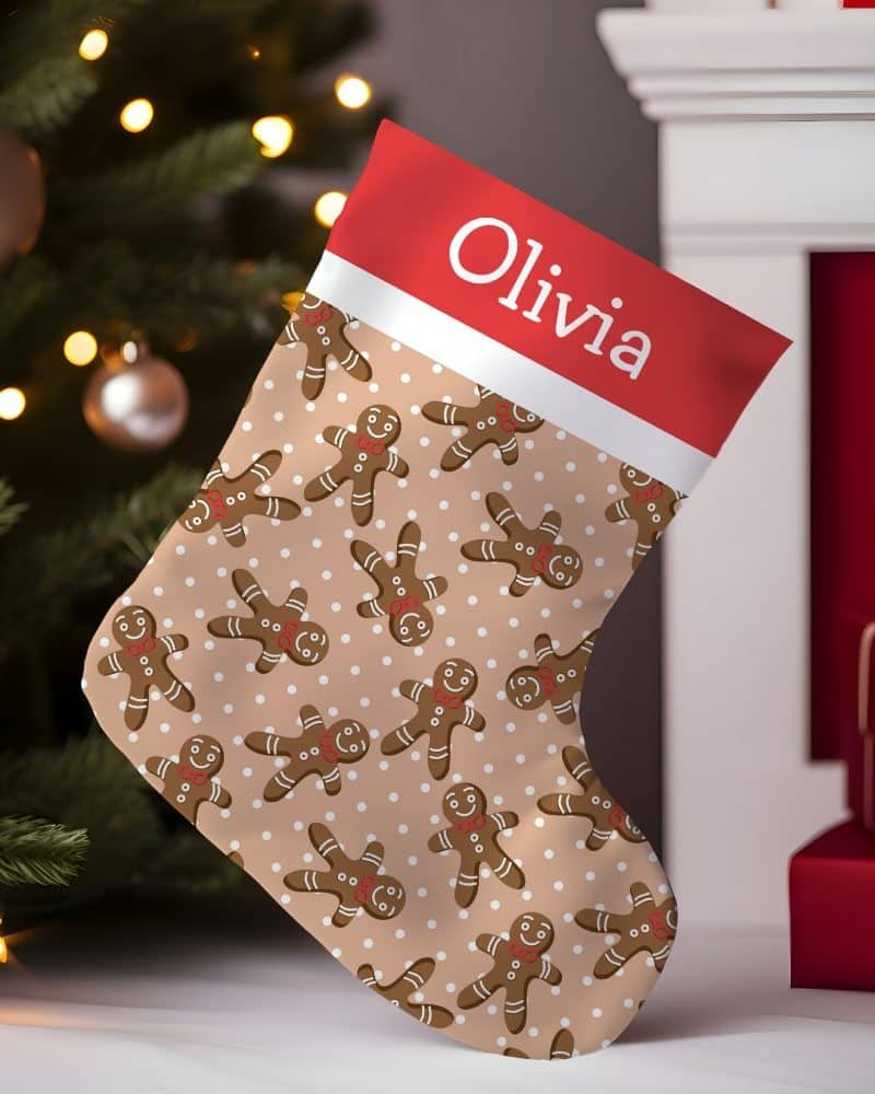 Personalized Christmas stocking with a beige background, featuring a repeating pattern of gingerbread men and white polka dots. The stocking's cuff is red and white, with the name Olivia printed on it.