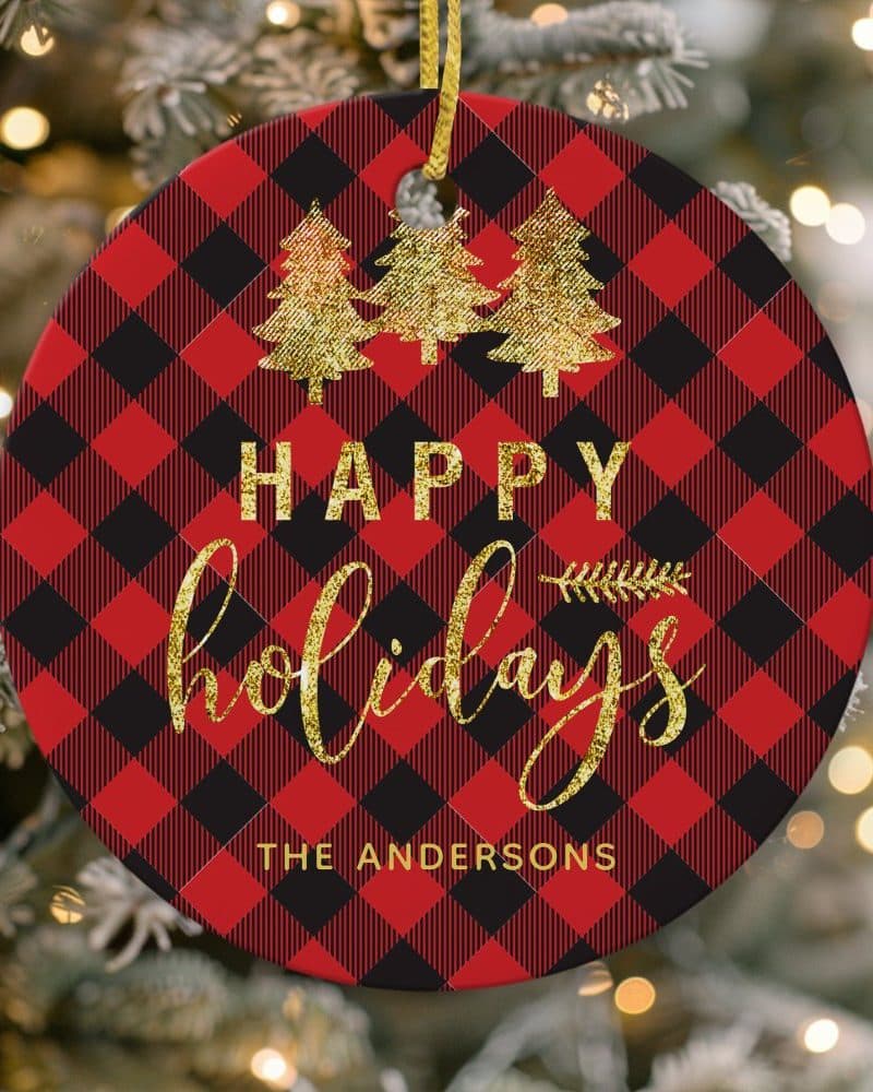 Round red and black buffalo plaid Christmas ornament with gold glitter Happy Holidays text and three gold glitter Christmas trees, personalized with The Andersons.