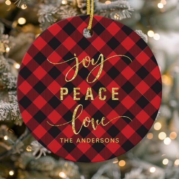 Round Christmas Ornament With Red And Black Buffalo Plaid Pattern, Gold Lettering That Reads Joy Peace Love, And The Andersons At The Bottom.