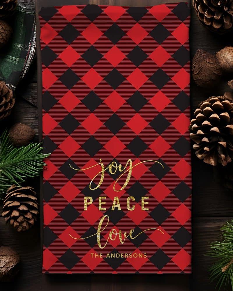 Red and black buffalo plaid Christmas tea towel with gold lettering reading Joy Peace Love and The Andersons.