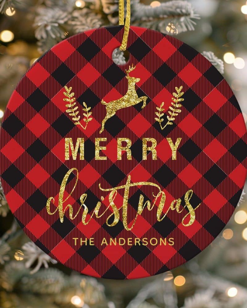 Round Christmas ornament with red and black buffalo plaid pattern, gold glitter reindeer, Merry Christmas text, and The Andersons family name.