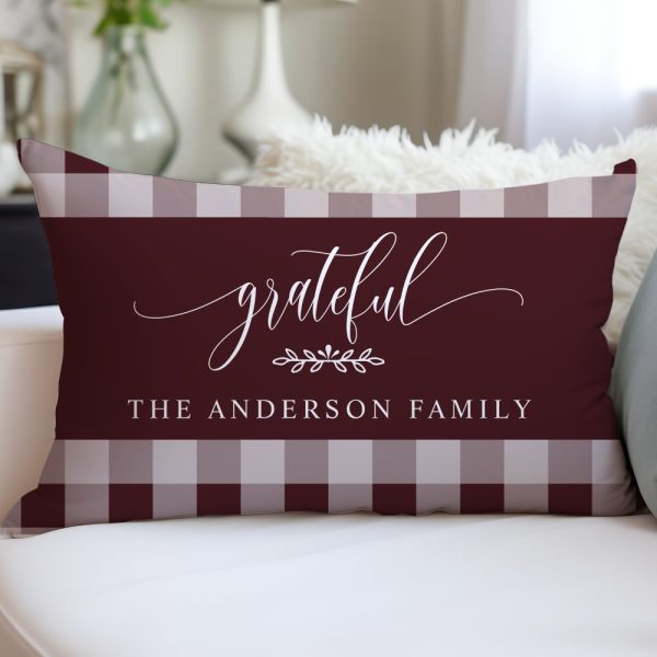 Burgundy Rectangular Pillow With A White Gingham Border And The Words Grateful, A Small Floral Design, And The Anderson Family In White Script.