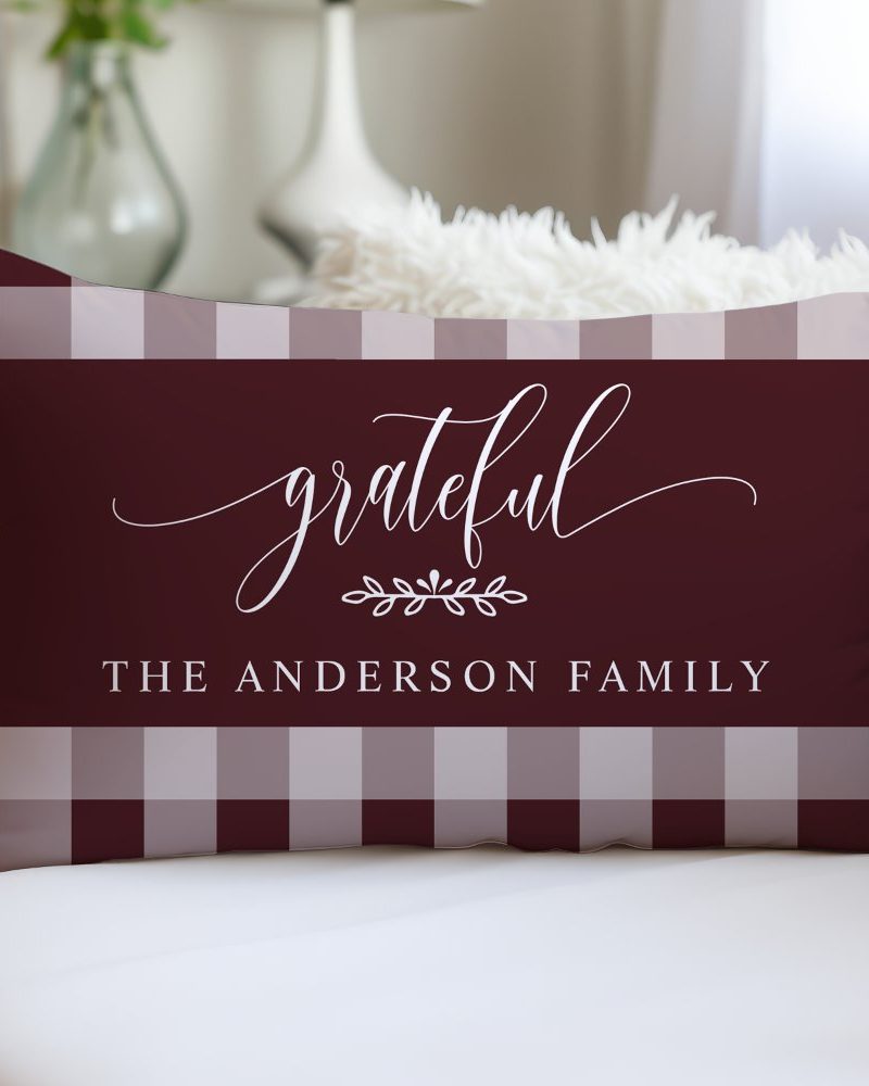 Burgundy rectangular pillow with a white gingham border and the words grateful, a small floral design, and The Anderson Family in white script.
