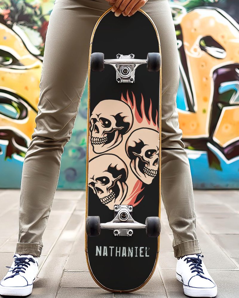 Person holding a skateboard with three skulls and flames graphic. The name Nathaniel is printed at the bottom.