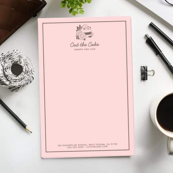Pink Stationery For Cut The Cake Bakery And Cafe. A Logo Of A Cake Is At The Top. Contact Information Is At The Bottom.