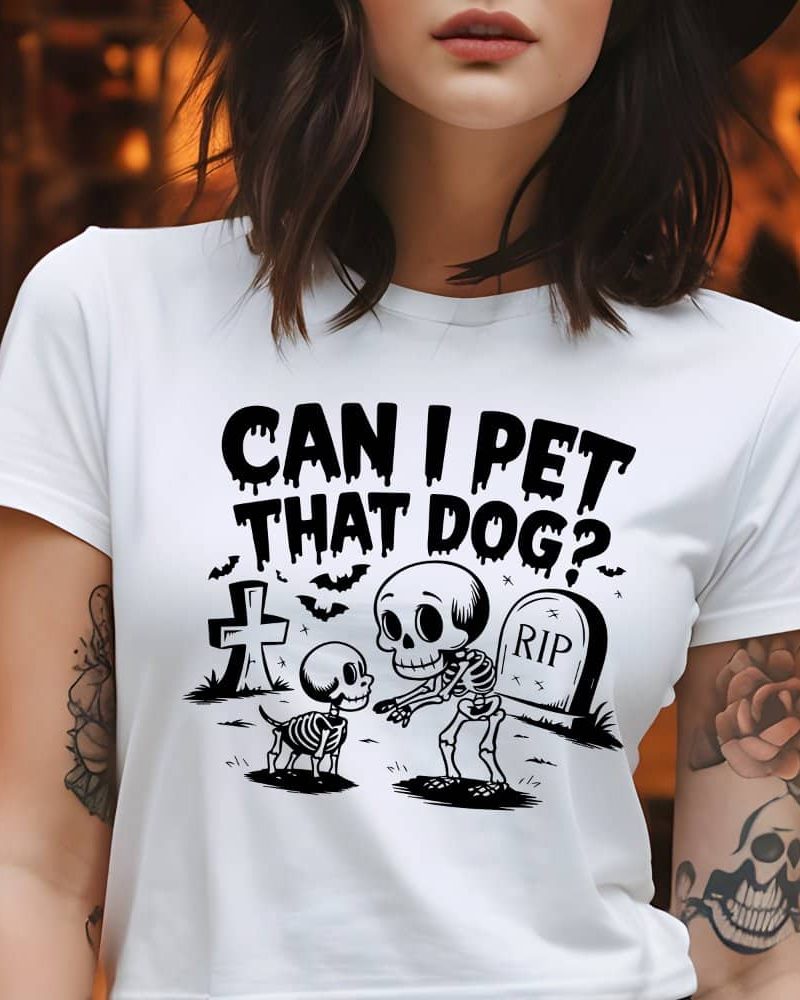 Woman wearing a white t-shirt with a Halloween design featuring skeletons of a dog and person, and the text Can I Pet That Dog?