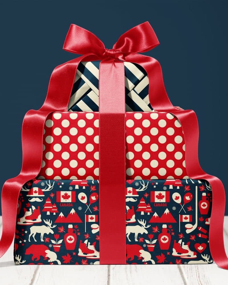 Stack of three presents wrapped in festive Canadian-themed paper, tied with a large red ribbon.