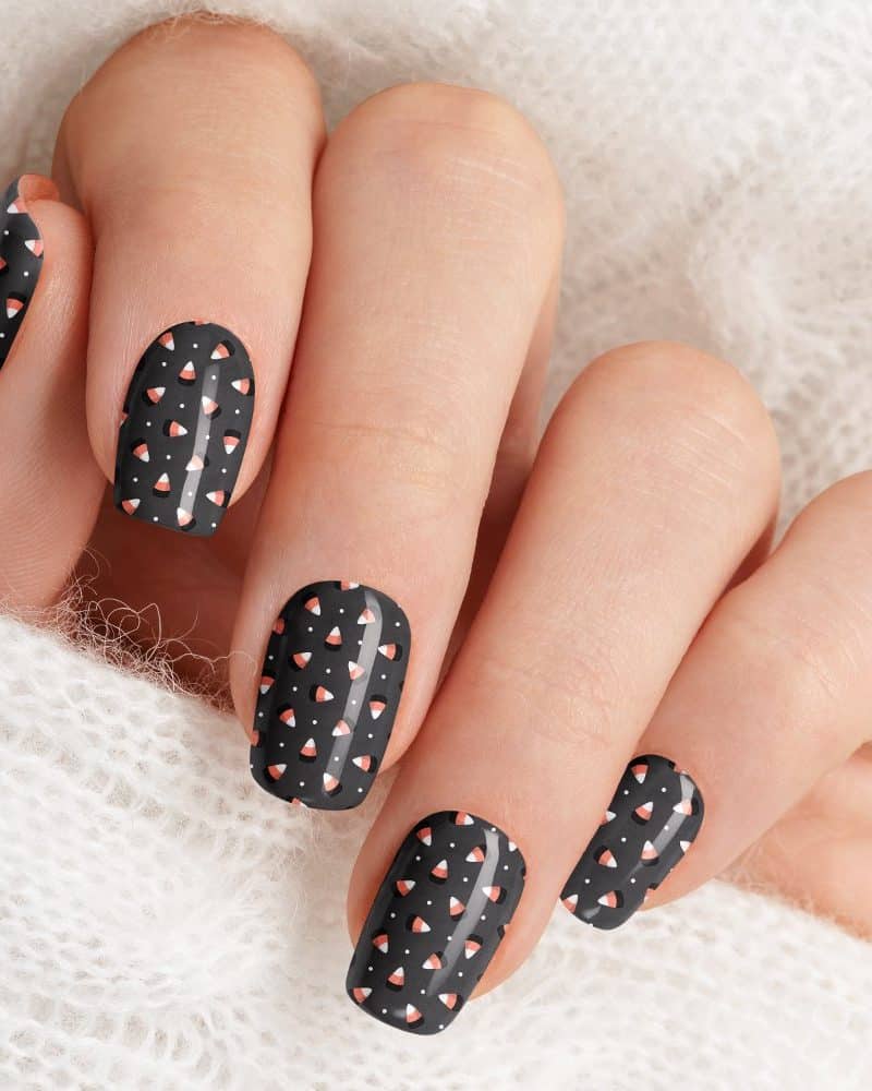 Close-up of a hand with black fingernails decorated with a small white and orange candy corn pattern.