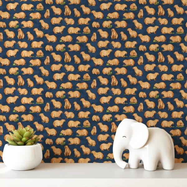 A Dark Blue Background Patterned With Repeating Images Of Capybaras. A Small White Elephant Figurine And A Succulent Plant Are In The Foreground.