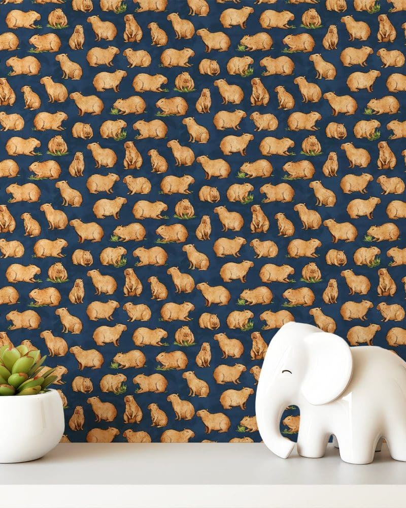 A dark blue background patterned with repeating images of capybaras. A small white elephant figurine and a succulent plant are in the foreground.