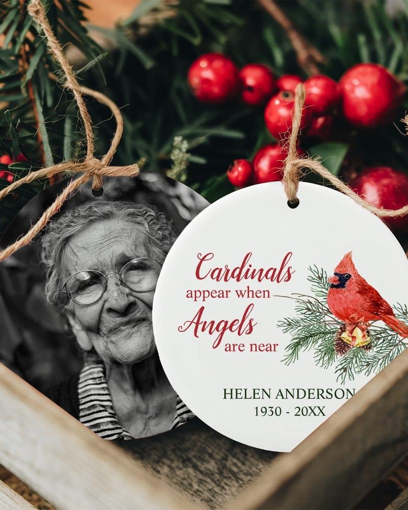 Two round Christmas ornaments. One features a black and white photo of an elderly woman. The other shows a cardinal on a branch with the text Cardinals appear when Angels are near, and a name and years.